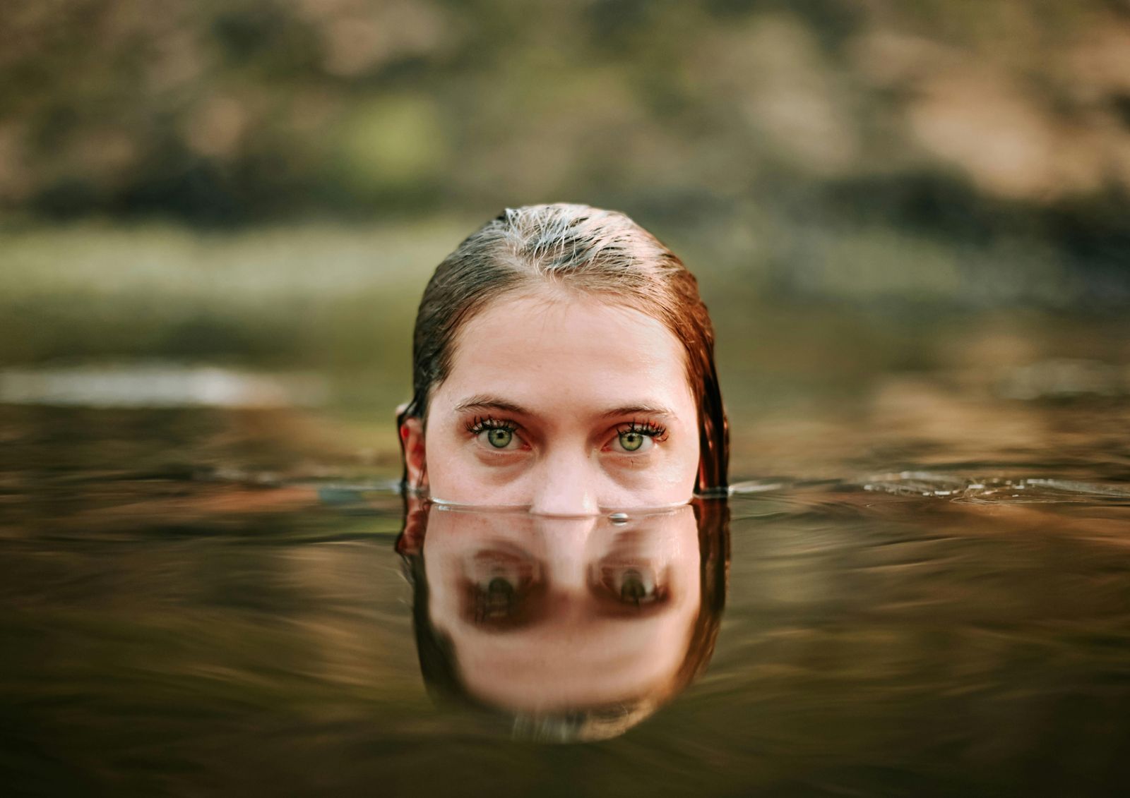 A face rising from a still green river — water and skin meeting the light